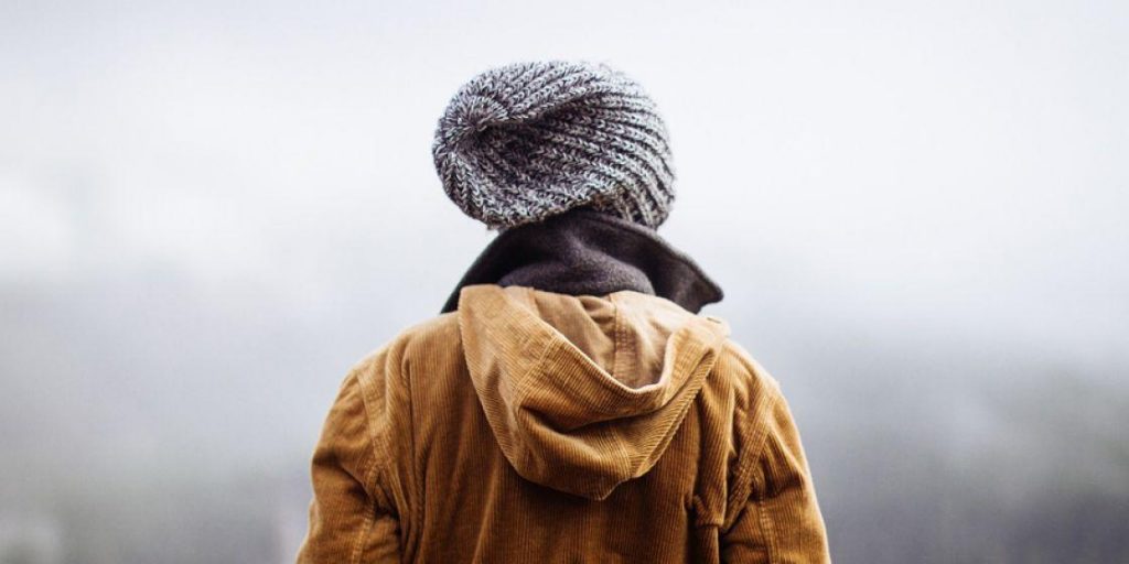 Persona de espaldas con abrigo y gorro frente a un paisaje cubierto de niebla.