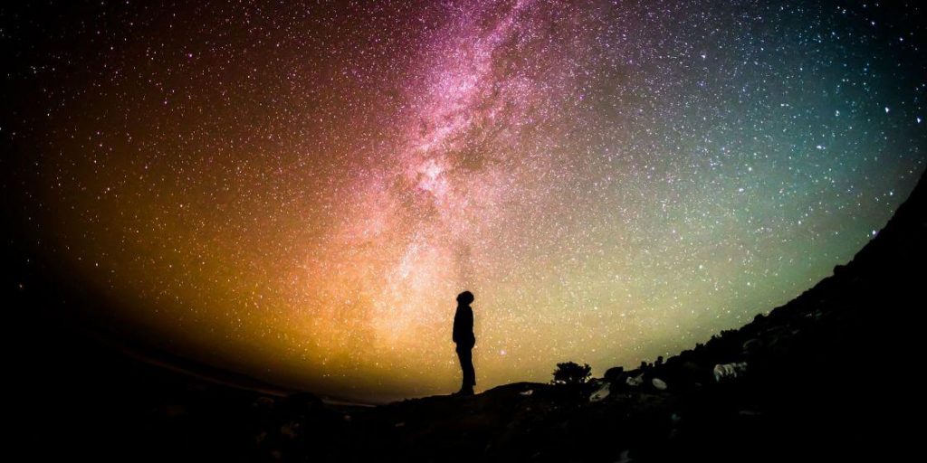 Silueta de una persona contemplando la Vía Láctea sobre un paisaje oscuro.