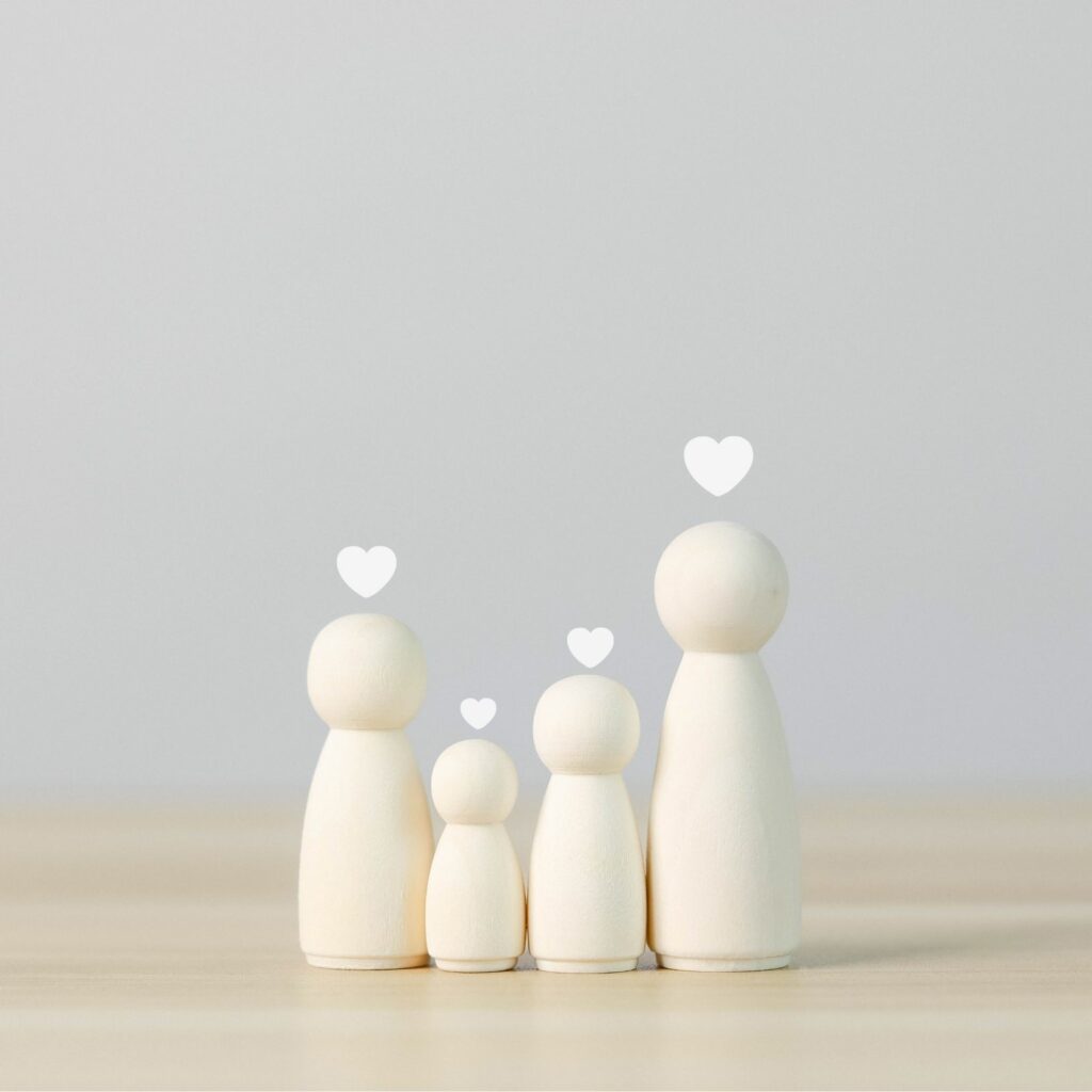 Cuatro figuras de madera de distintos tamaños representan una familia, con un corazón sobre cada una.